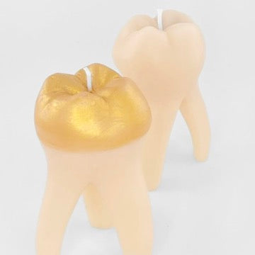 Two tooth-shaped candles on a plain light background, one with a metallic gold crown and one in a natural off-white shade.
