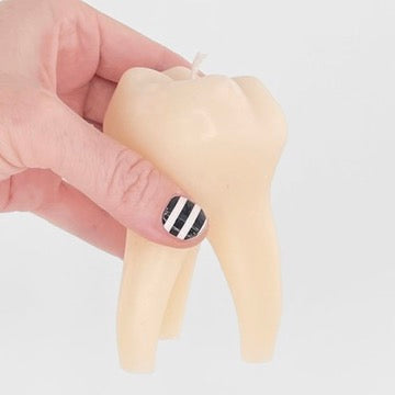 A hand holding a novelty tooth-shaped candle against a plain light gray background.
