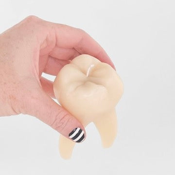 A hand holding a novelty tooth-shaped candle against a plain light gray background.