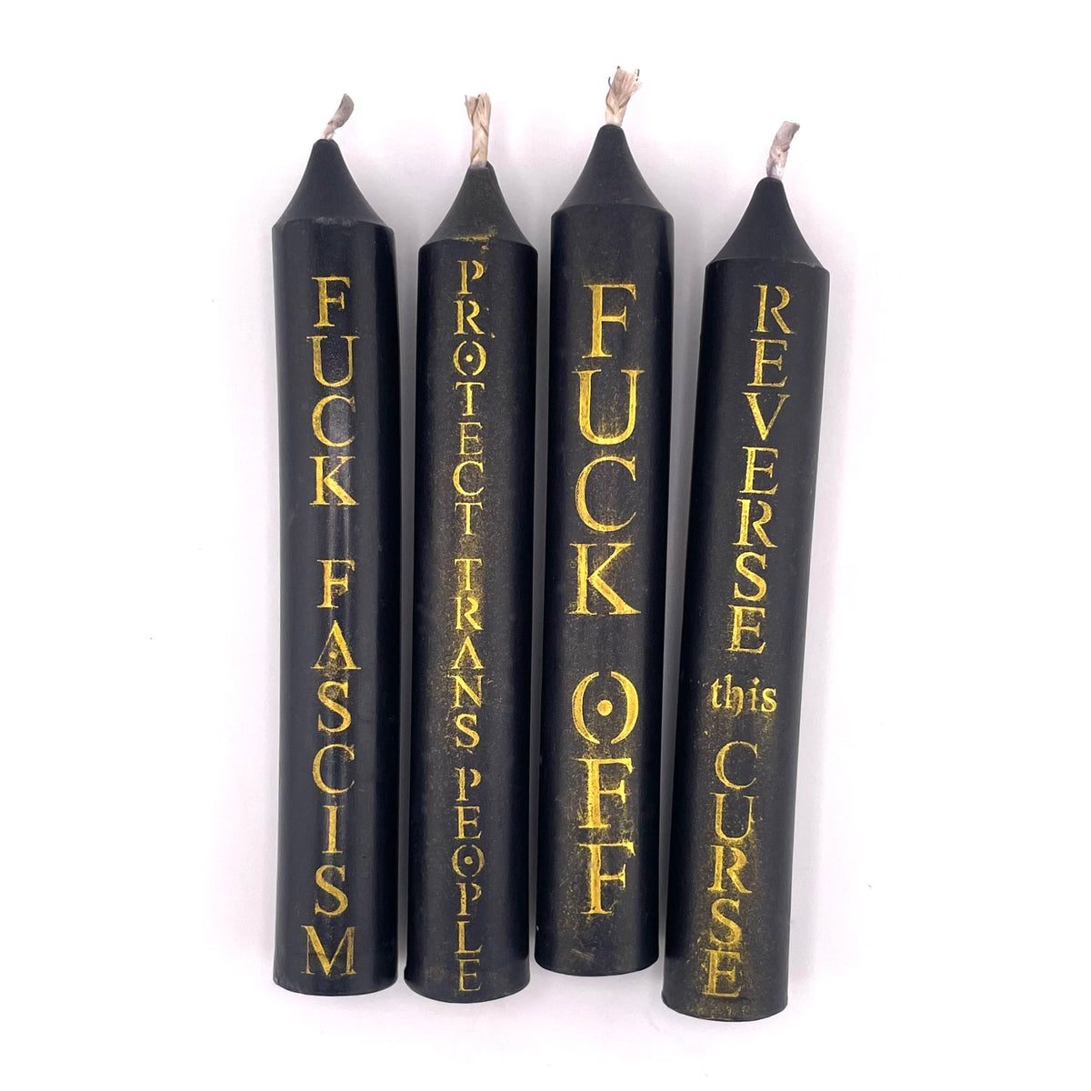 Four black candles with gold text on a white background reading "FUCK FASCISM", "PROTECT TRANS PEOPLE", "FUCK OFF". and "REVERSE THIS CURSE."