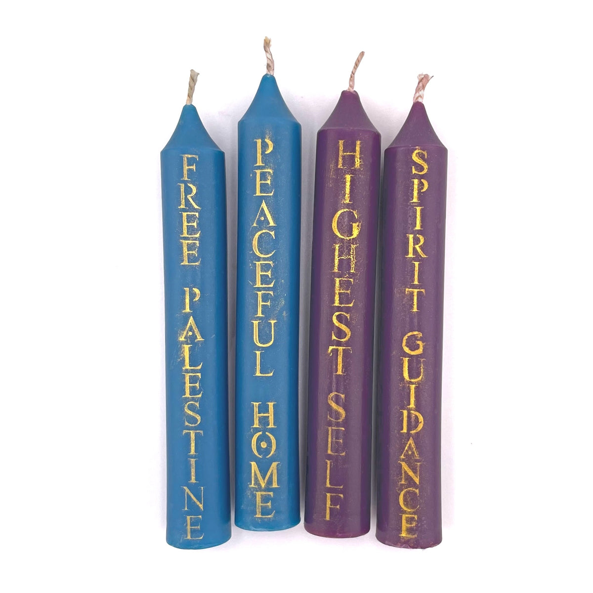 Four taper candles with gold text on a white background. Two are blue and read 'FREE PALESTINE' and 'PEACEFUL HOME'. The other two are purple and read 'HIGHEST SELF' and 'SPIRIT GUIDANCE'.