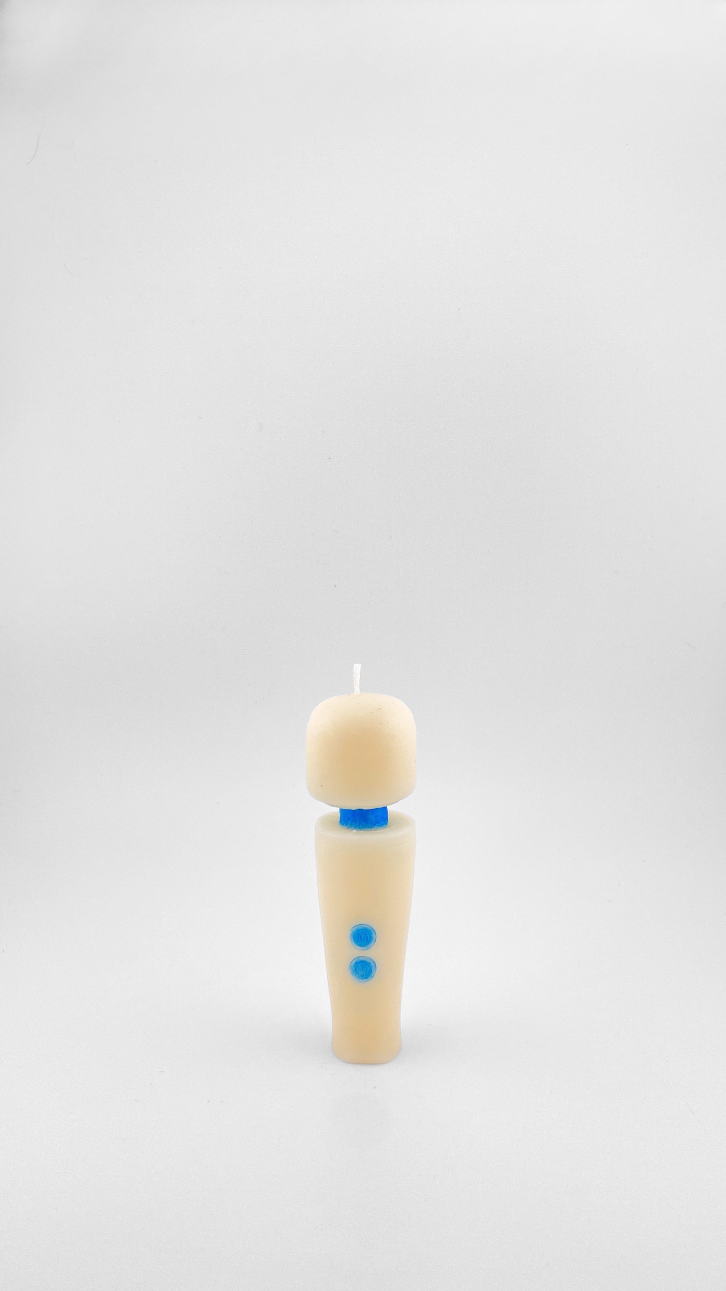 A small candle in off-white soy wax with a small blue collar and two blue buttons resembling the iconic Magic Wand Vibrator, standing on a white background.