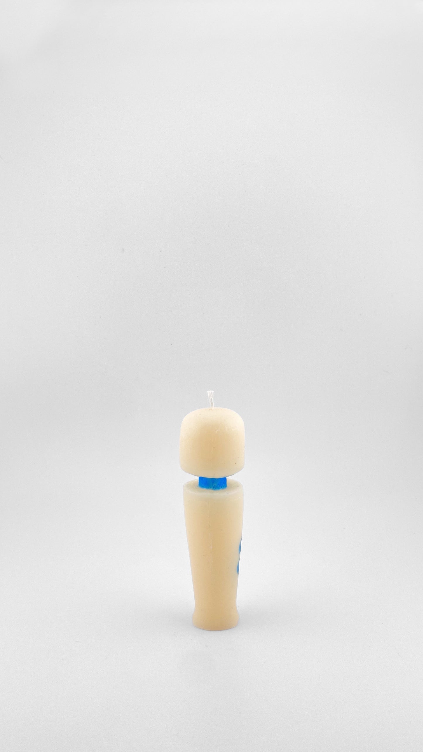A side view of a novelty candle shaped like the iconic Magic Wand vibrator, in off-white soy wax with a small blue neck and buttons, set against a plain light gray background.